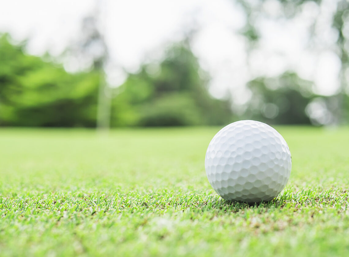 golf ball green with blurred pin flagstick green tree background